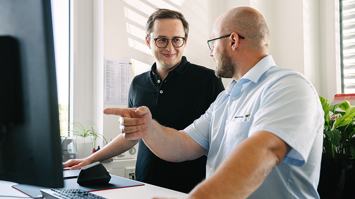 Zwei Mitarbeiter stehen am Computer und beraten sich.